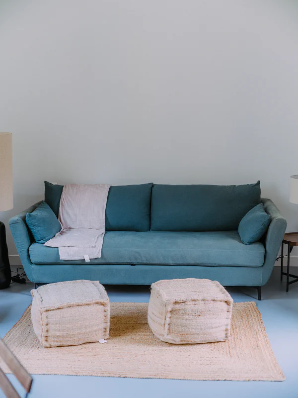 Canapé bleu canard avec poufs en jute sur tapis naturel dans l'appartement du château