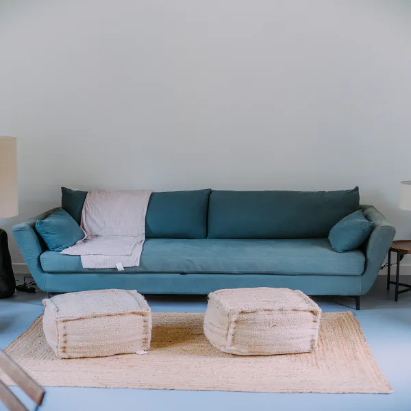 Canapé bleu canard avec poufs en jute sur tapis naturel dans l'appartement du château