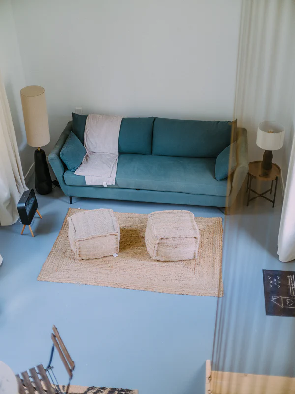 Salon de l'appartement vu depuis la mezzanine avec canapé bleu et poufs en jute