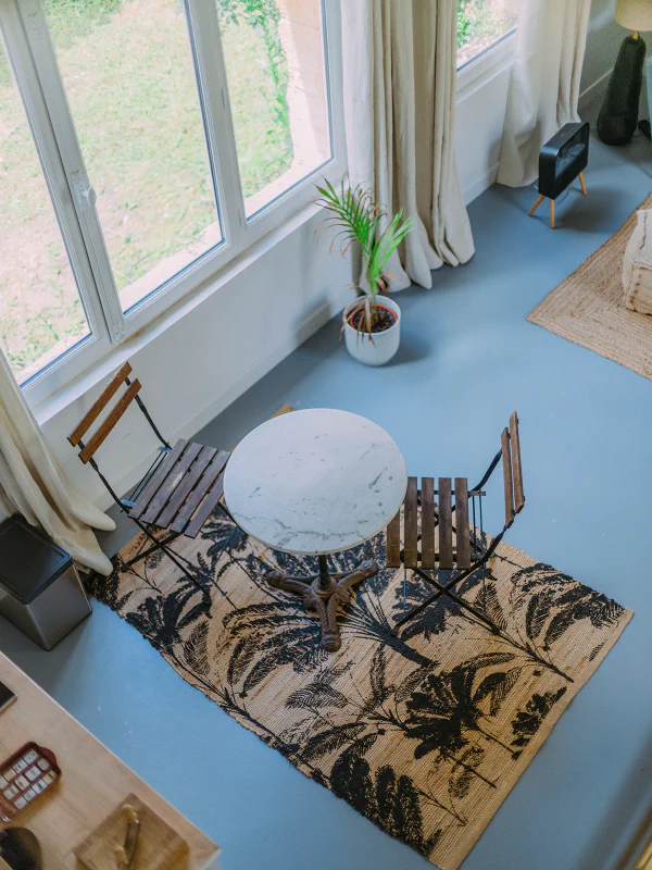 Coin repas vu de la mezzanine avec table bistrot et tapis tropical au château