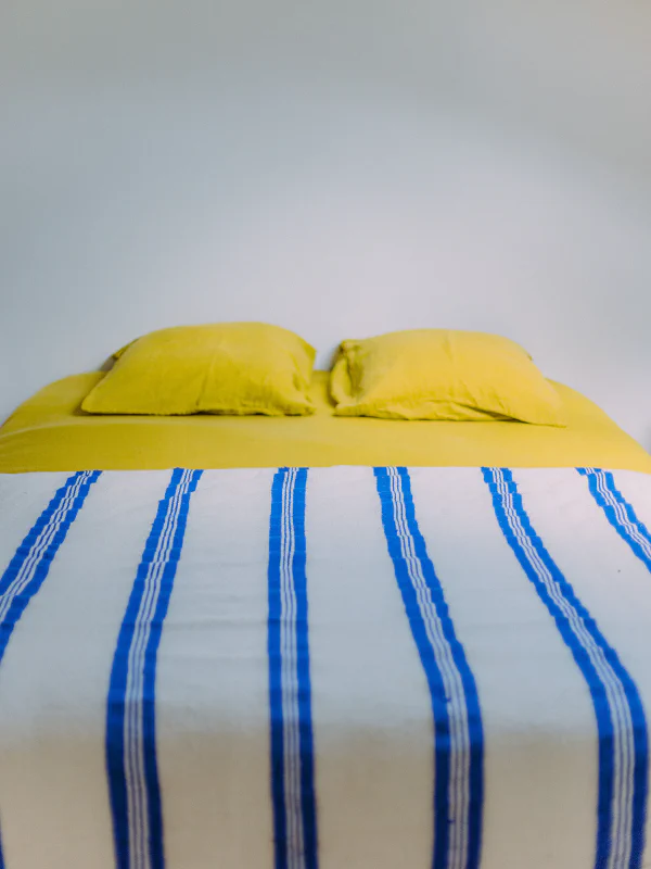 Lit double avec oreillers jaunes et couverture rayée bleue dans le gîte du château