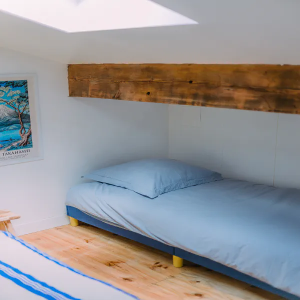 Lit simple sous poutres avec draps bleu ciel et vélux dans la mezzanine du château