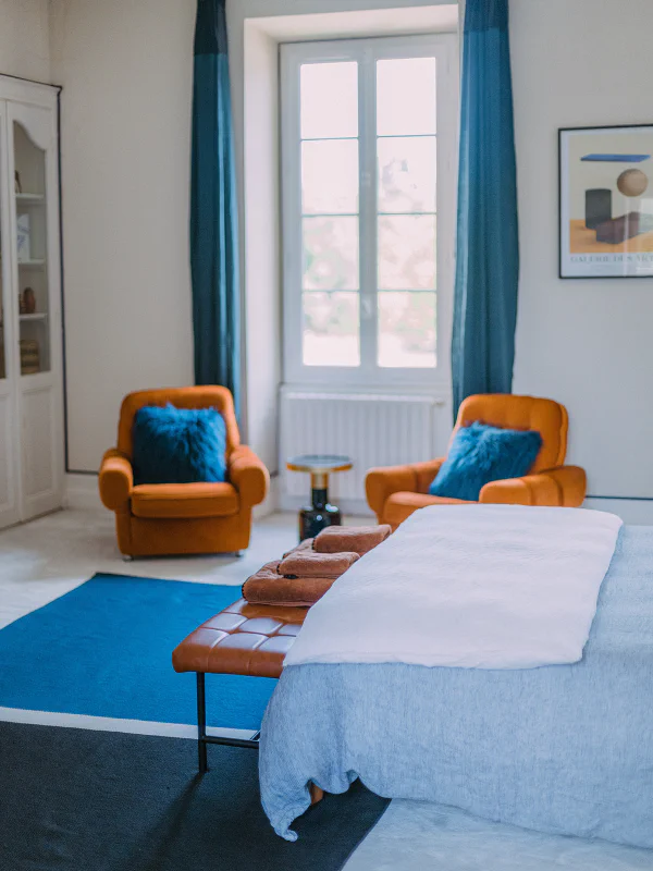 Chambre bleue avec fauteuils cuir cognac, rideaux bleu canard et banquette au château