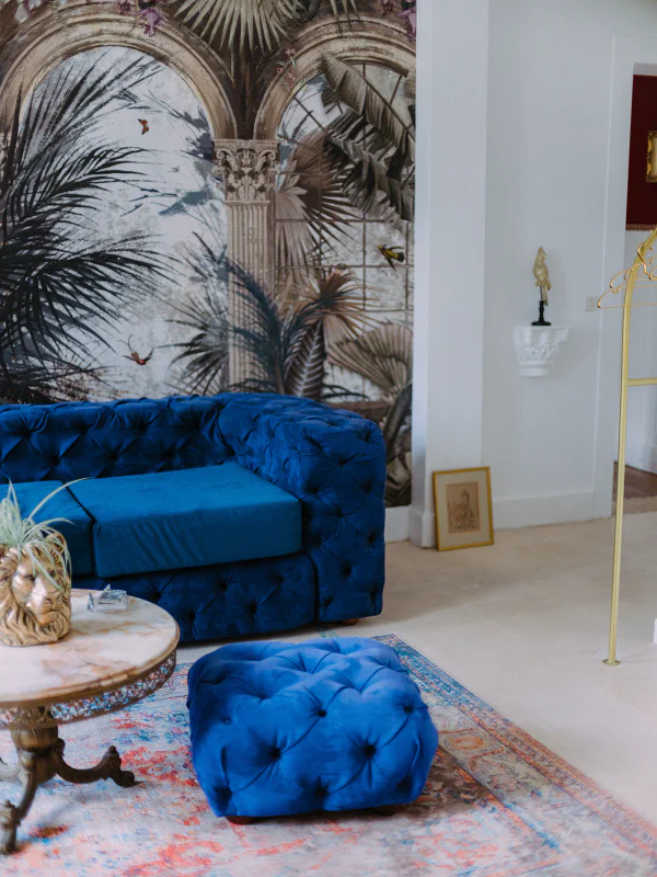 Canapé bleu capitonné et pouf devant fresque tropicale au Château de Laubardemont