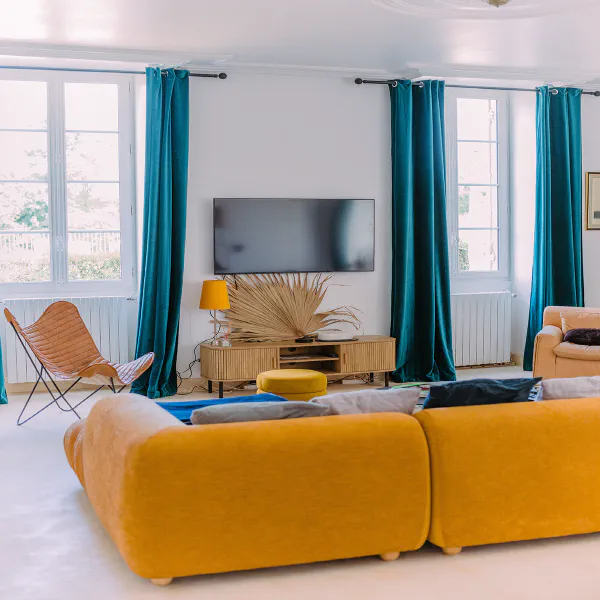 Vue panoramique du salon avec canapé moutarde et grandes fenêtres au château