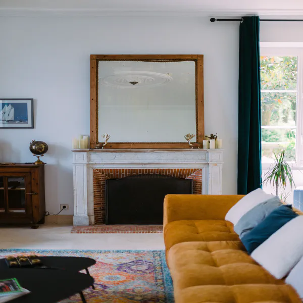 Cheminée en marbre blanc avec miroir ancien et canapé moutarde au Château de Laubardemont