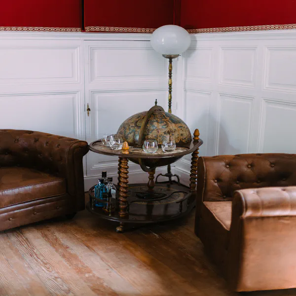 Bar globe vintage entre canapés Chesterfield en cuir marron au Château de Laubardemont